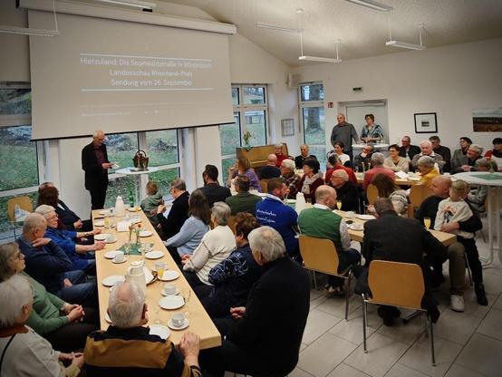 Besucherinnen und Besucher des Neujahrsempfangs im Gemeindesaal an Tischen. Vorne Ortsbürgermeister Friedhelm Kunz.