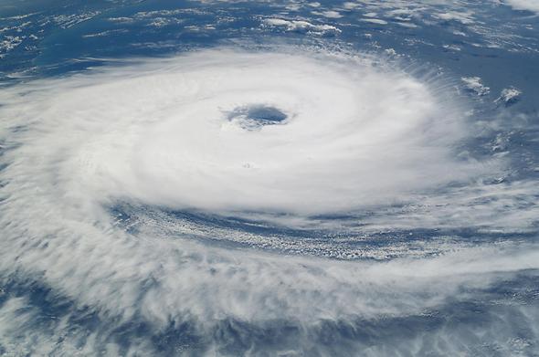Image of a hurricane, visible through white cloud vortices, from above.