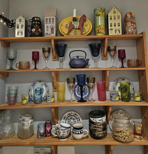 Assorted coloured glassware, blue and white china, and painted tins arranged pleasingly on open kitchen shelves against a duck-egg-blue wall.