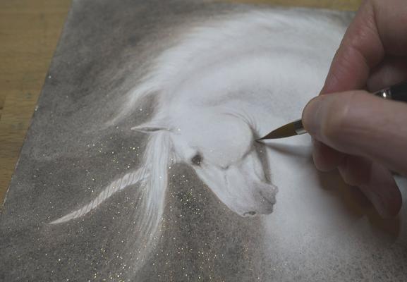 watercolour painting of the head and neck of a unicorn in a dark brown pigment which gives it a sepia effect. You can see my hand in the image painting it and the reflection of the sparkling gold that is scattered throughout this otherwise drab pigment. Magic!