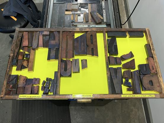 Top-down photo of a wood letterpress typecase containing pieces of broken wud type on top of neon yellow drawer lining