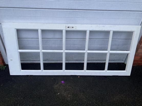 A white wooden door is leaning horizontally against a white garage door. It is unglazed but has the framework to accommodate ten panes.
