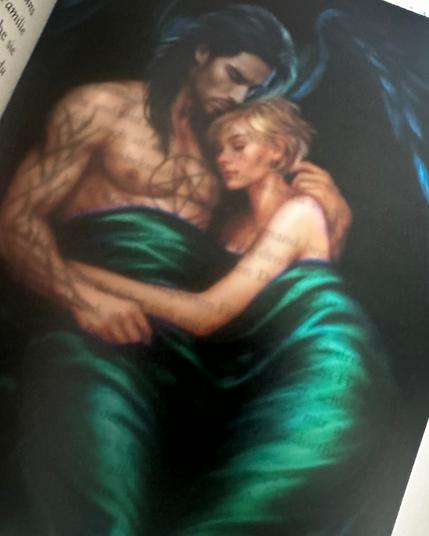 Ein Foto von einem Page-Overlay im Buch, auf dem die Hauptcharaktere (Mann und Frau) gezeigt werden. Beide kuscheln nackt unter einer grünen Decke. Beim Mann handelt es sich um einen Engel mit schwarzen Flügeln.