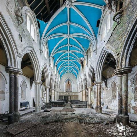 interior of an abandoned church, featuring a striking blue arched ceiling. Debris litters the floor of this once sacred and central to worship.