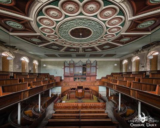The photo shows the interior of an old church with a grand pipe organ. The ceiling is ornately decorated with circular patterns