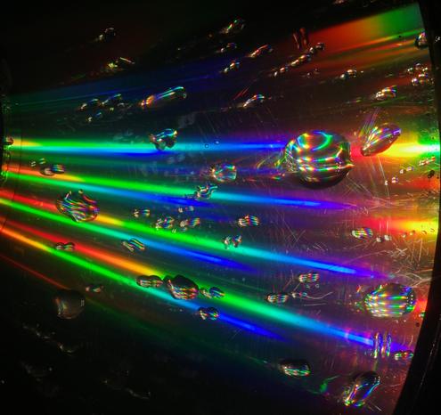 A wet CD was illuminated with white LED light during the night. The CD surface refracts the light, and the resulting rainbow colours are reflected in the droplets.
