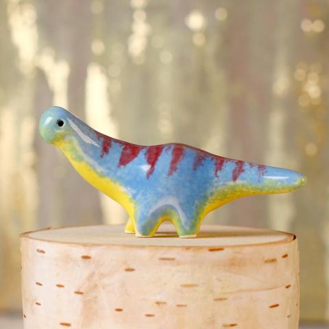 A small blue ceramic dinosaur with a yellow belly and red stripes.