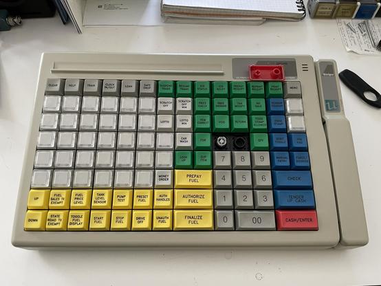 A point of sale keyboard with keys in grey, yellow, green, red, and blue with various labels related to operating a gas station. There’s also a credit card swipe slot on the right.