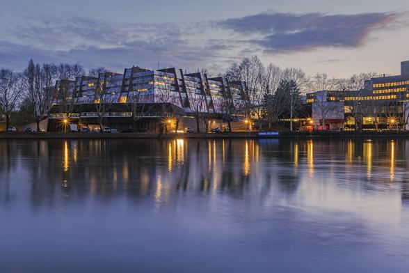 Council of Europe's modernist building and its reflection on Ill river in Strasbourg during a winter evening. The sky is turning to pale purple and buildings windows are lit with warm ligths.