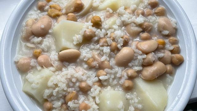 Un plato de potaje blanco con garbanzos, judiones, patatas y arroz.