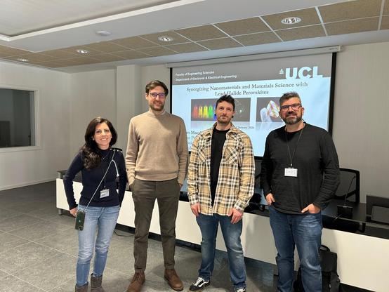 Group photo taken after the invited seminar at INAM–Universitat Jaume I. Dr. Tom Macdonald stands with members of the INAM research community in a lecture room. Behind them, a projected slide shows the seminar title “Synergizing Nanomaterials and Materials Science with Lead-Halide Perovskites” and the UCL logo.