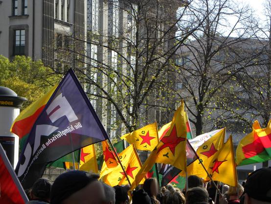 Demonstration mit Flaggen der nord-ost-syrischen Miliz YPG und eine Flagge der FAU im Vordergrund