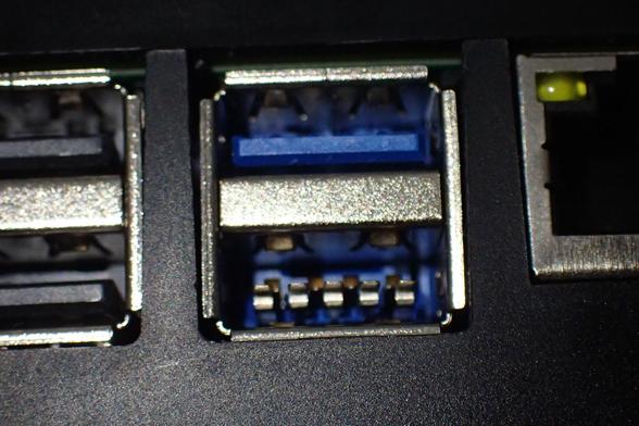 Schnittstellen am Raspberry Pi 5, schwarzes Kunststoffgehäuse. In der Mitte sind die USB3-Ports, erkennbar am blauen Kunststoff bei den Pins. Beim unteren Port fehlt diese Kunststoffplatte, da stehen die Pins frei heraus. Links sieht man noch zur Hälfte die USB2-Ports mit grauem Kunststoff, rechts den halben Ethernet-Port.