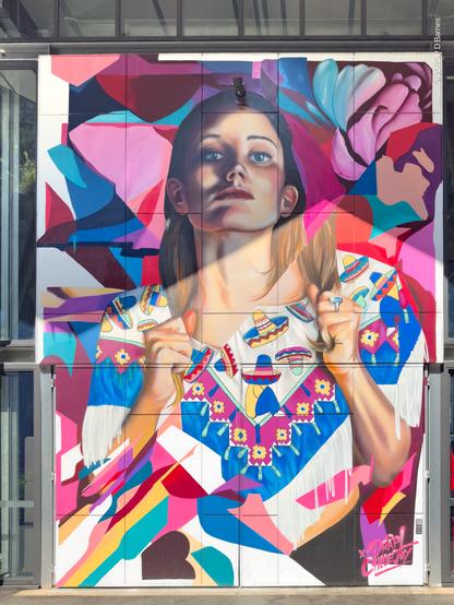 Colourful portrait of a young woman wearing a shirt with mexican motifs, against an abstract pink, purple and blue background. On the wall of a barrel hall, riverside, Brisbane.