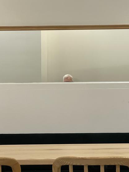 A colour photo of a white-headed man in a mirror. Only his forehead and white hat are visible. The mirror is landscape long and there are other long horizontal lines, including a table.