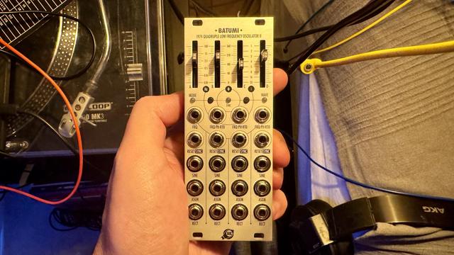 The image features a hand holding a modular synthesizer module labeled "BATUMI," which is identified as a quadruple low-frequency oscillator. The module includes various knobs and jacks for frequency and wave selection.