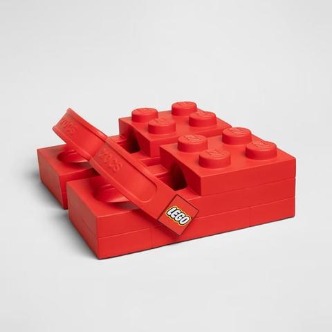 A pair of red Crocs designed to resemble LEGO bricks, featuring raised studs and a LEGO logo. The Crocs are stacked and positioned on a neutral background.