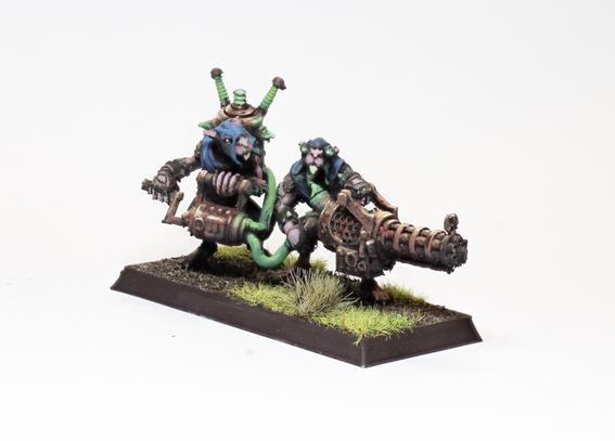 A pair of ratmen holding a hand cranked minigun in blue attire. A sickly green glow pulses from the warpstone shards embedded in the weapon.
