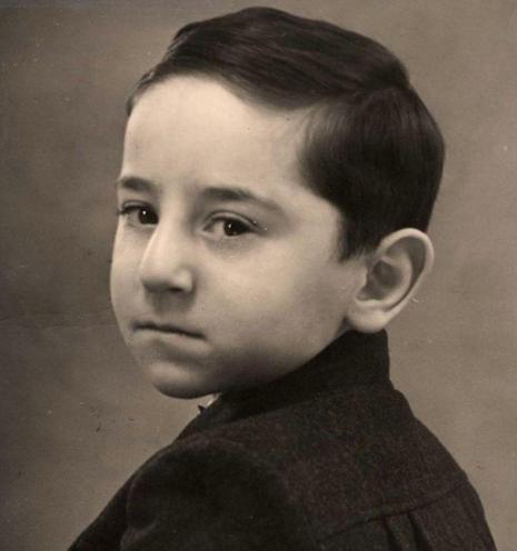 Vintage black and white portrait of a young boy with short dark hair. He is wearing a dark jacket and turns his head towards the camera.