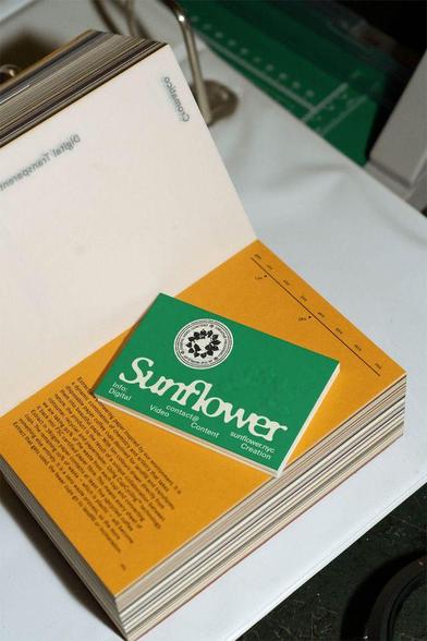 A close-up of a stack of colorful printed sheets, featuring a green card for "Sunflower" with digital content information.