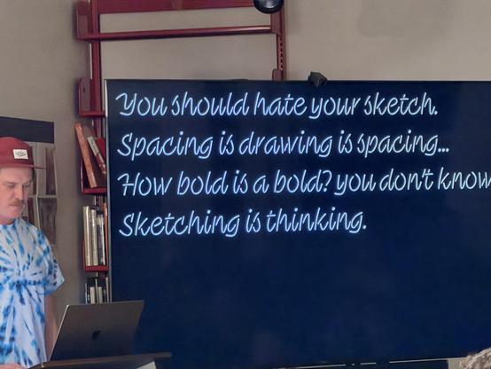 Photo of a man presenting to a room. On the screen are the sentences:
You should hate your sketch.
Spacing is drawing is spacing...
How bold is a bold? You don’t know. 
Sketching is thinking.