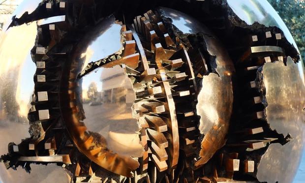 a shiny bronze sculpture that looks like a sphere inside a sphere with lots of gears