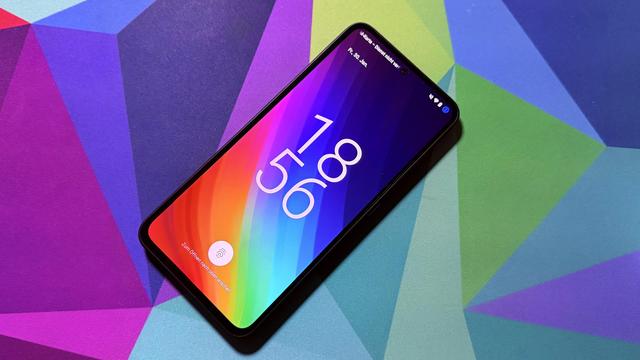 Ein gesperrtes Nothing Phone mit aktivem Bildschirm und buntem Hintergrundbild auf einer bunten Unterlage.