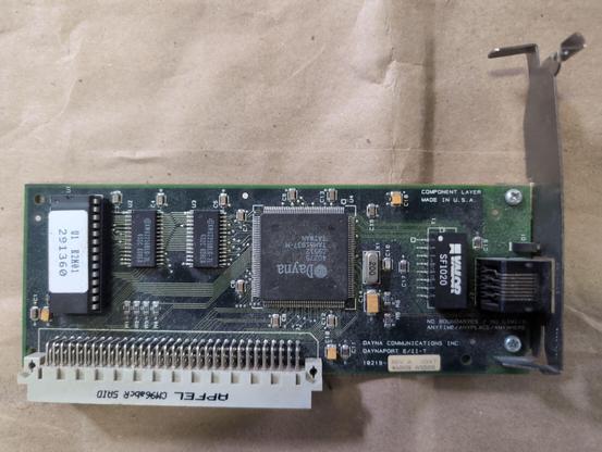 A very small NuBus card with a single external connector. The largest chip has Dayna printed on it. In the lower right Dayna Communications Inc Daynaport e/11-t is screenprinted. No boundaries/no limits/anytime/anyplace/anywhere.