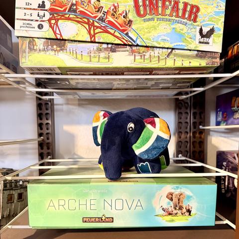 Tideways PHP elePHPant plushy on boardgame shelf between „Ark Nova“ and „Unfair“.