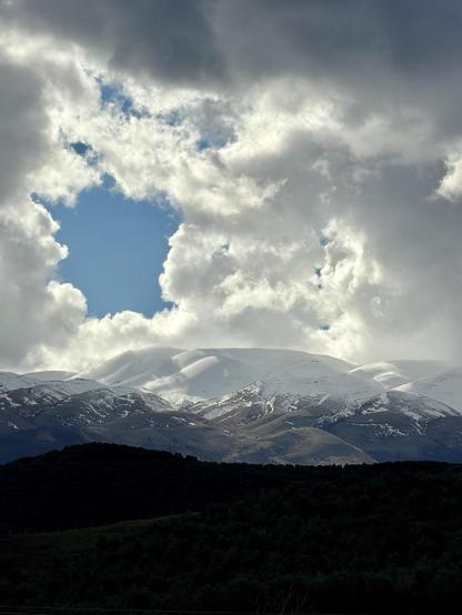 A piece of blue sky through a square hole in the clouds over the snow capped Albanian alps.