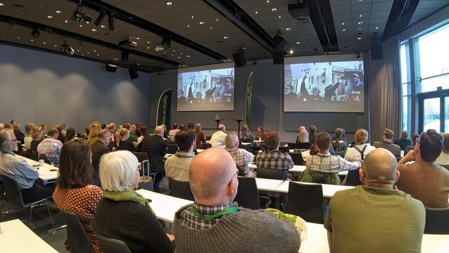 Deler av en fullsatt sal. På skjermene foran er musikkvideoen til Streets of Minneapolis, med bilde av demonstranter med plakat som sier Fuck ICE