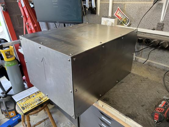 Three quarters view of a large metal box sitting on a workbench (other side).