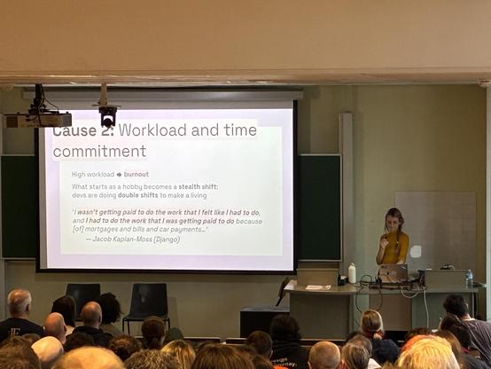 Miranda on stage next to a slide about Workload and time commitment