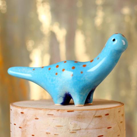 A small light blue ceramic dinosaur with a dark blue belly and orange polka-dots.