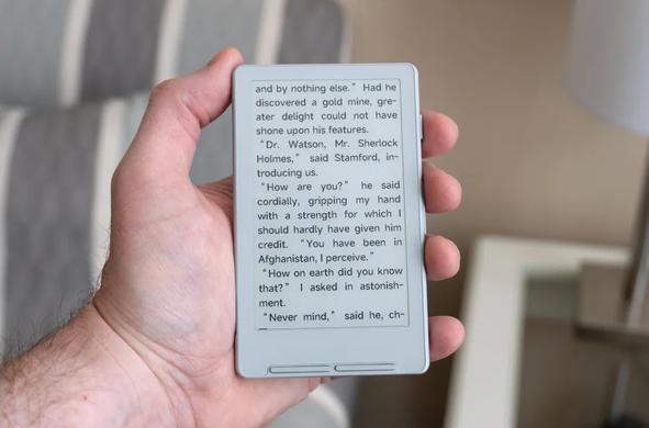 Photo of Xteink X4 ebook reader held in a human hand. It's silver-grey and about "palm-sized".