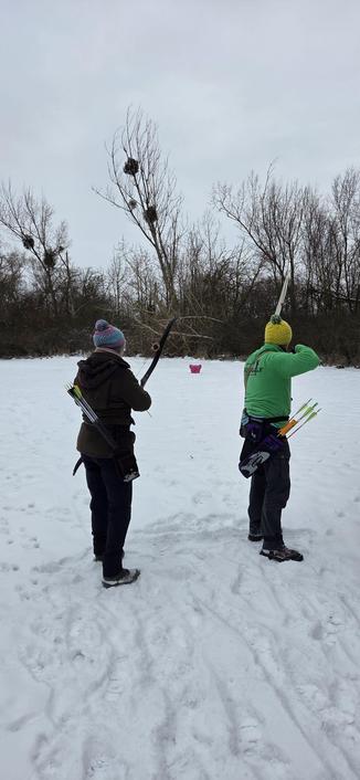 Zwei Bogenschützen stehen im Schnee und zielen auf ein im Schnee stehender Arsch mit Ohren in roter Farbe