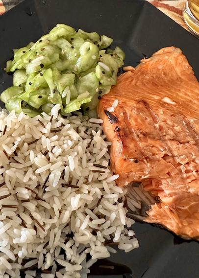 A plate of teriyaki salmon with a side of wild rice and cucumber tsukemono.