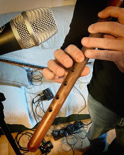 Hands playing a Duduk (Armenian flute) in front of a microphjone. On the background we can see cables, a small mixer and an echo FX pedal