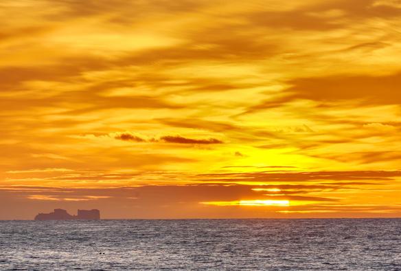 Sunset along the west Antarctic Peninsula. An iceberg can be seen next to the setting sun.