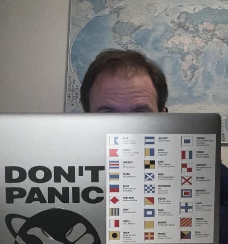 Photo of me behind my laptop with a sticker on it, displaying the international maritime signal flags