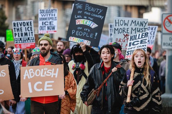 A photo of a dense crowd of protesters holding anti-ICE signs including "REVOKE THE ICE PERMIT - ICE OUT OF PORTLAND!" and "THE BEAUTY OF THIS COUNTRY LIES IN THE DIVERSITY OF IT'S PEOPLE!" and "ABOLISH ICE!" marching down a city street.