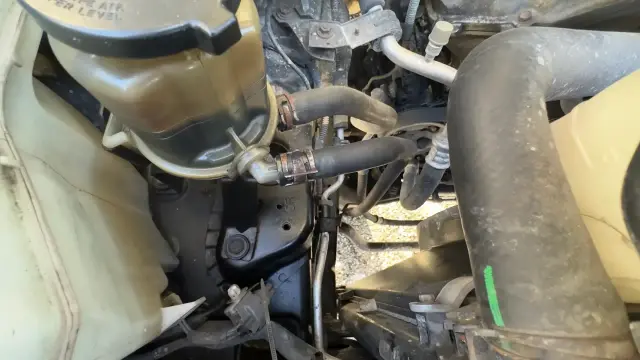 Power steering reservoir on a 2007 Toyota FJ Cruiser showing the return and feed hoses and hose clamps.