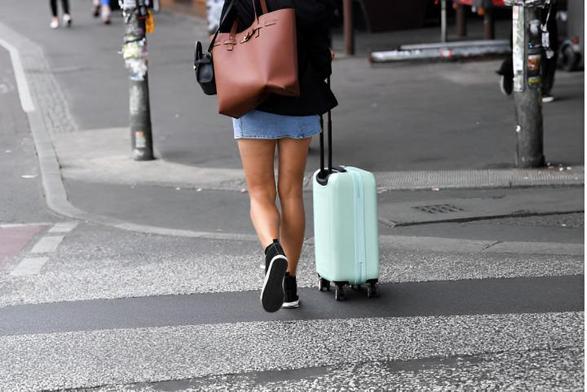 Una mujer caminando con una maleta azul por la calle. (Getty Images)