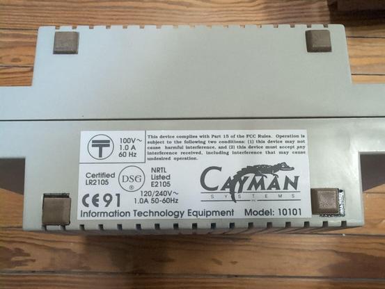 The bottom of the enclosure with four rubber feet and a sticker with voltage (100 V, 60 Hz; 120/240 V, 50-60 Hz) and FCC info. The Cayman Systems logo with cayman is printed on it above Information Technology Equipment Model 10101.