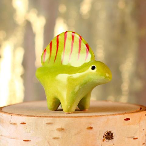 A small green ceramic dimetrodon with a light green belly and red stripes.
