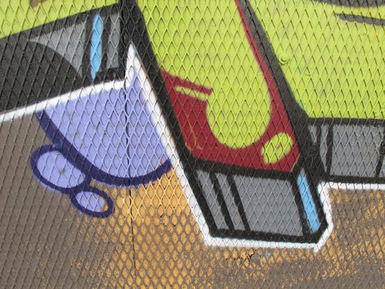 Bold graffiti with neon green, maroon, yellow, and lilac purpose in vaguely organic but geometric shapes over a plywood wall that is covered with a perforated metal sheet in a diamond pattern.