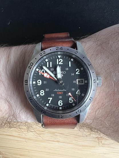 A Seiko 5 GMT field watch with a black dial strapped to my wrist using a brown leather strap.