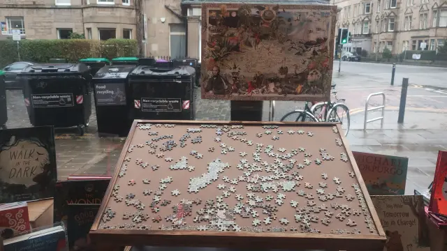 An angled puzzle table in the Edinburgh Bookshop window, with a partly completed jigsaw of Charles Darwin's voyages on it