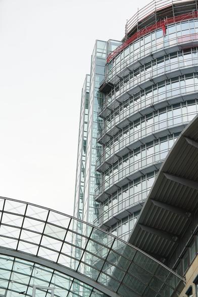 Gerundeter Glasturm mit außen liegenden Fahrstuhlschächten, darunter Glasdach