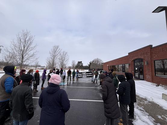 people gathered in a large circle in a small parking lot outside St Albans VT ICE facility